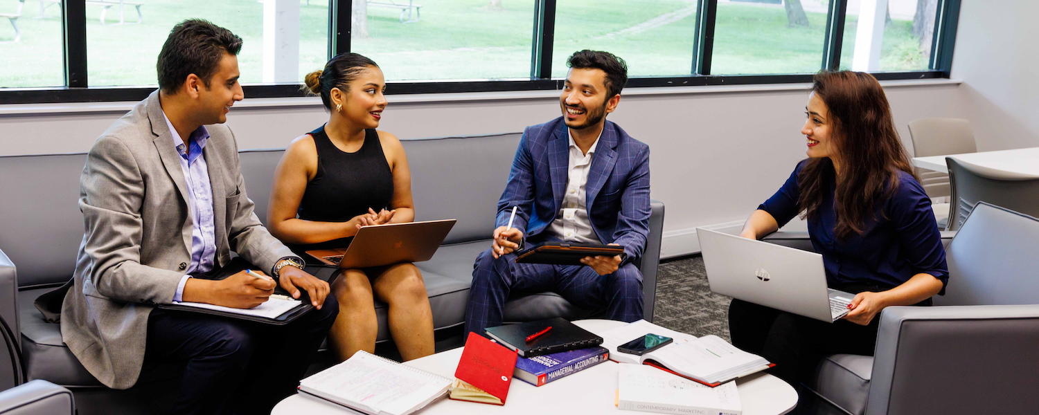 A group of four students with laptops sitting around a table with textbooks on it.