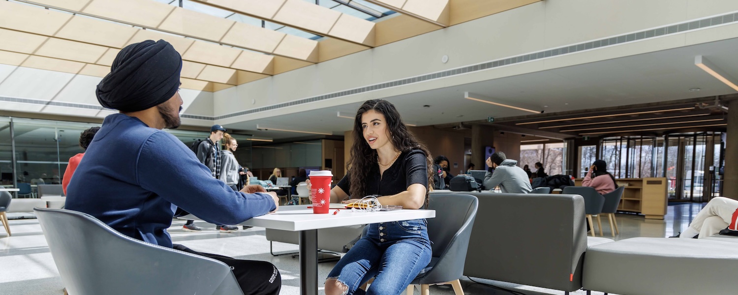 Two students sitting at a table in Brock University's Rankin Family Pavilion atrium.