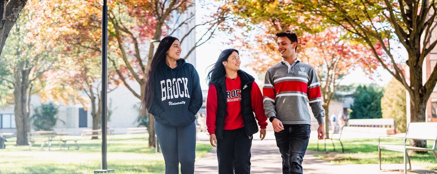 Three students walking on Brock University's main campus with colourful fall leaves in the background.