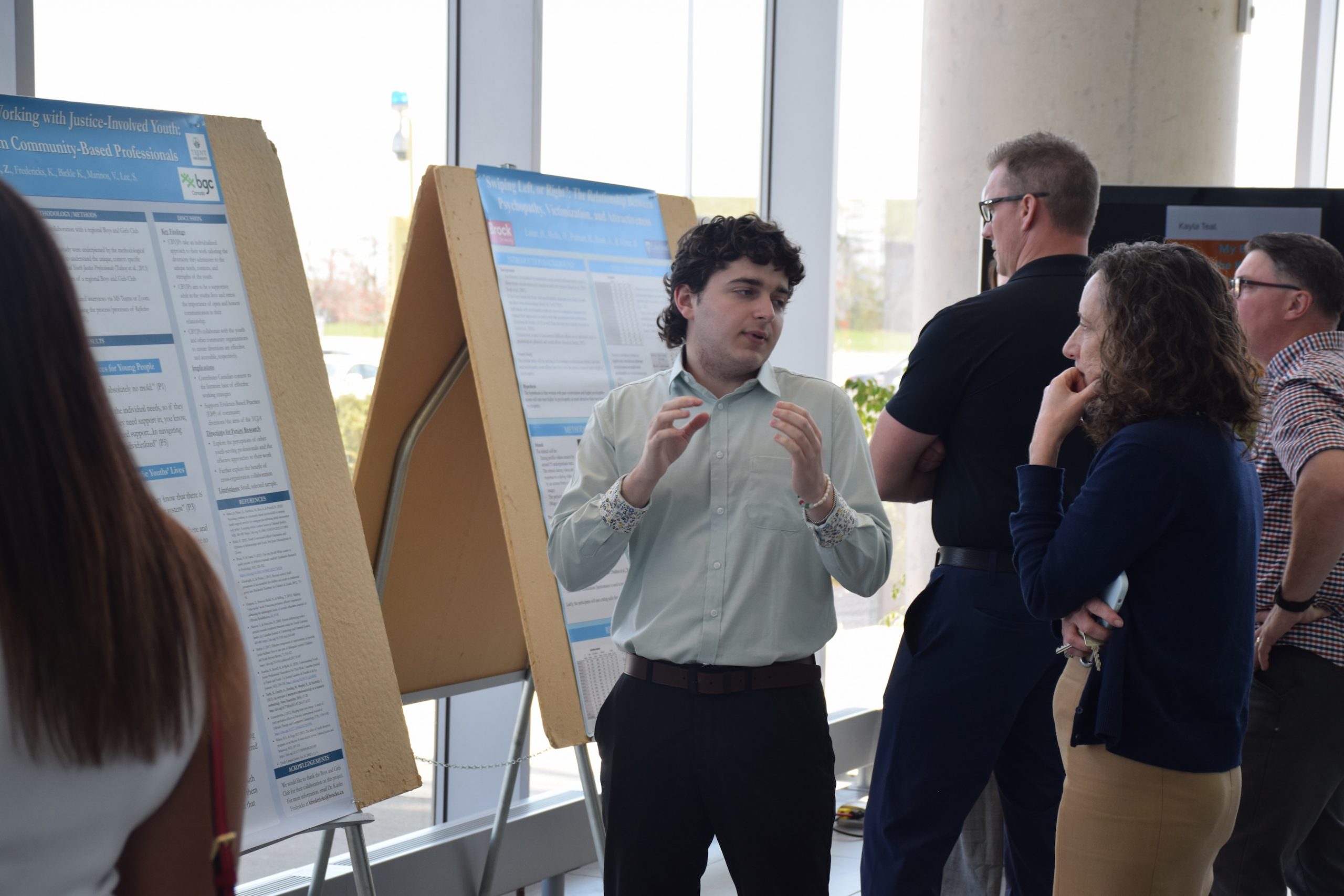 Two people having a conversation in front of a research poster with two other people in the background looking at another research poster.