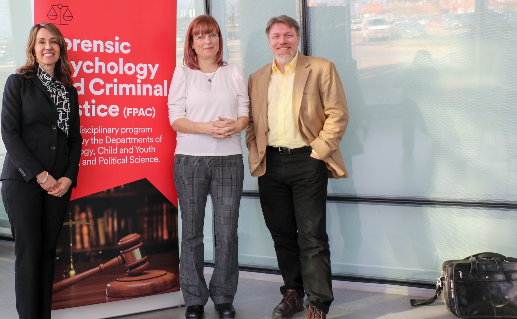 Three people stand in front of a Forensic Psychology and Criminal Justice pull up banner.