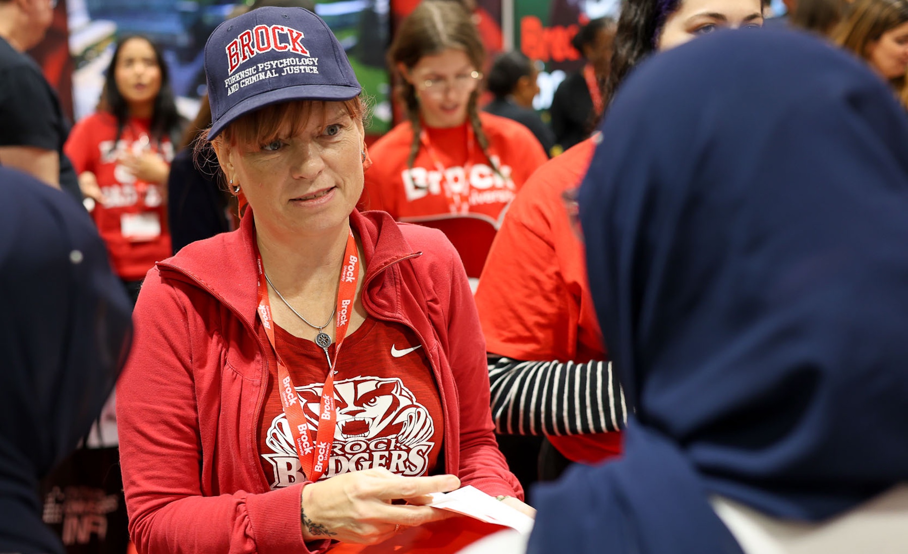 Someone in a Brock Forensic Psychology and Criminal Justice baseball hat talking to someone at an event.