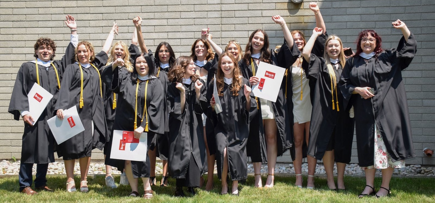 A group of students in academic robes cheer outside after a university graduation ceremony.