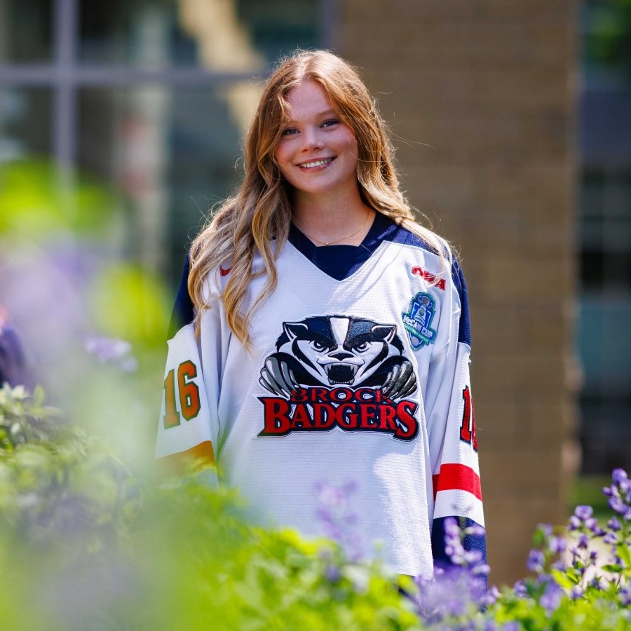 A young woman in a hockey jersey stands outside in a garden.