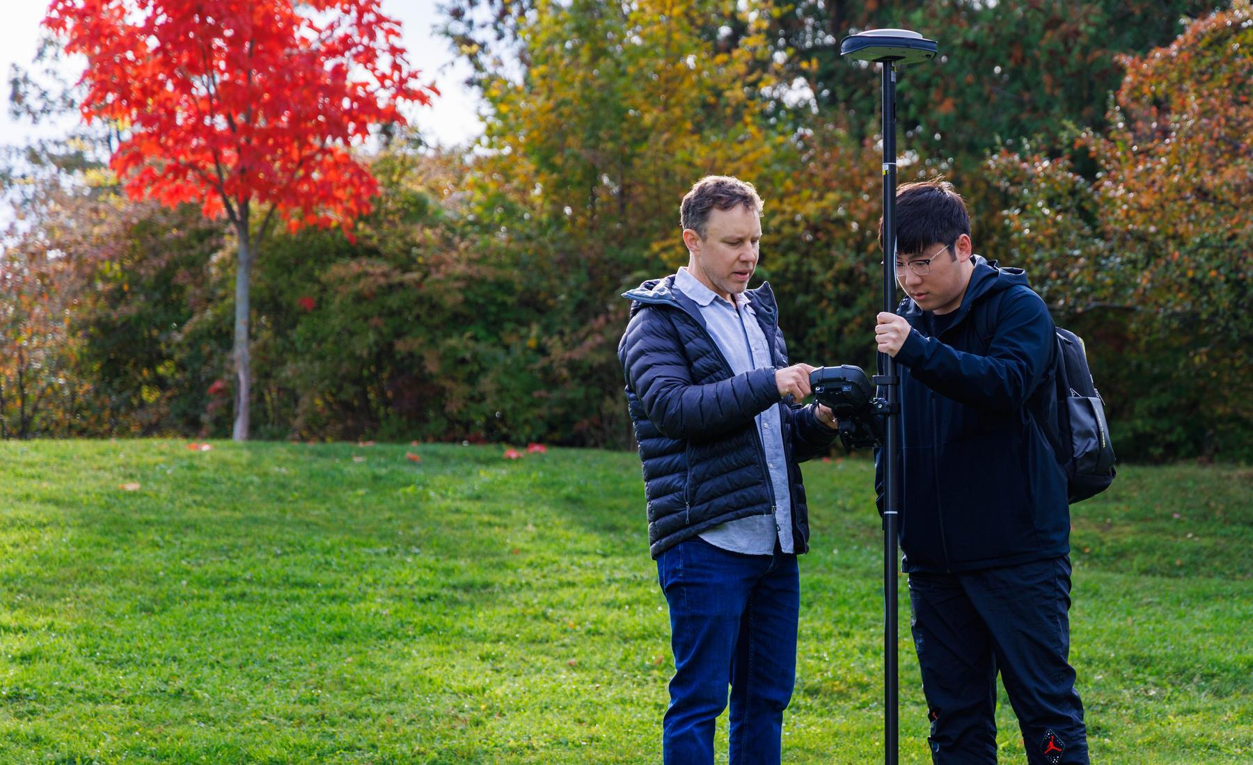 Kevin Turner and a student stand outside using 3D survey and digital mapping tools. 