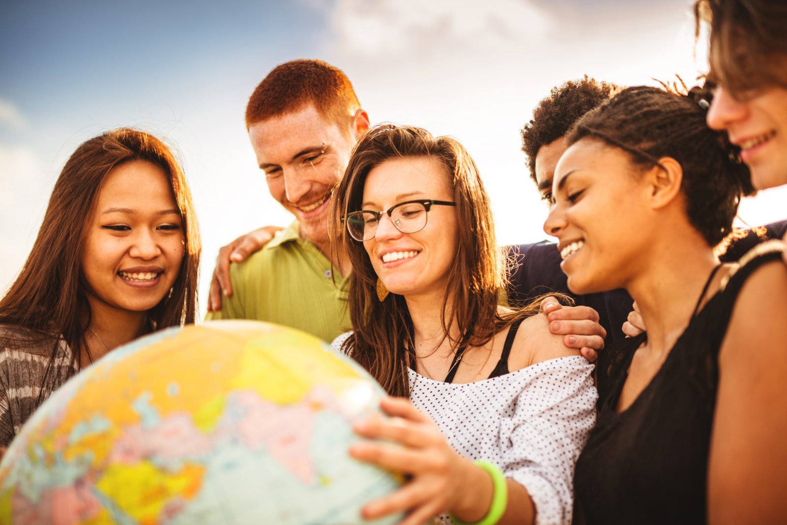 University students stand outside on a sunny day holding a globe.