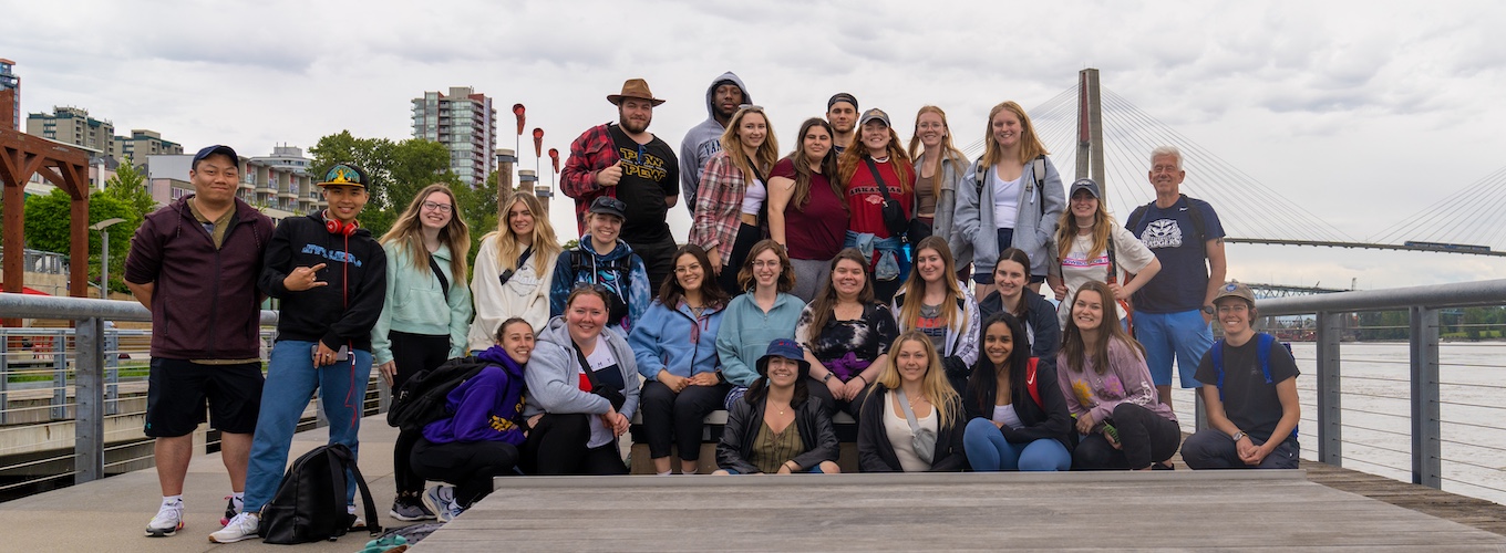 Students pose on boardwalk with Michael Ripmeester in front of a city skyline and bridge.