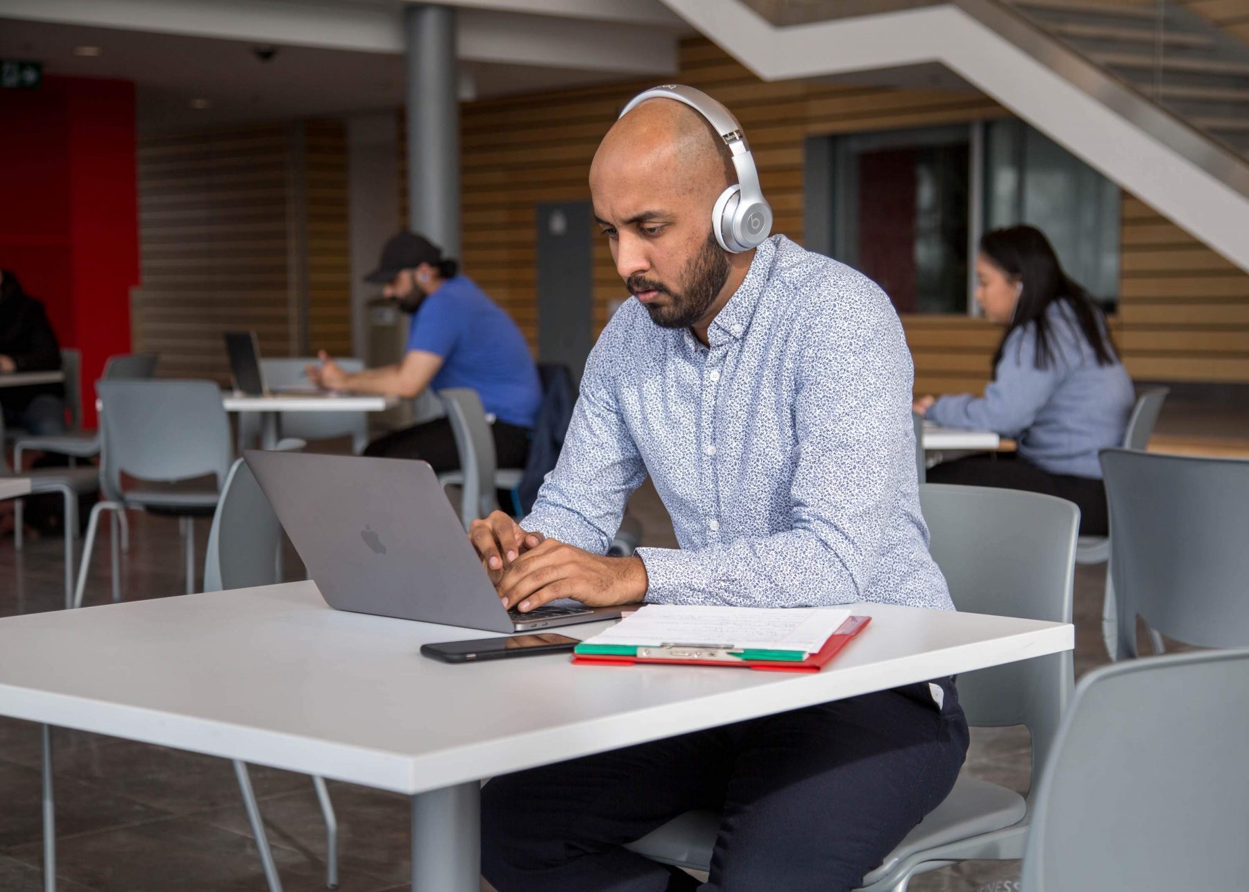 A person who's wearing headphones sits at a table and types on a laptop.