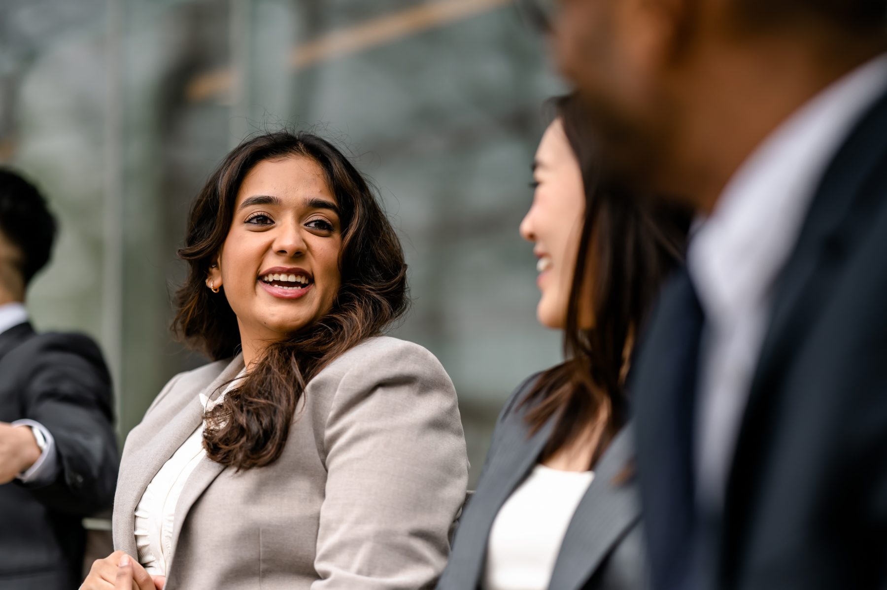 A group of people in business suits sitting on a bench and talking.