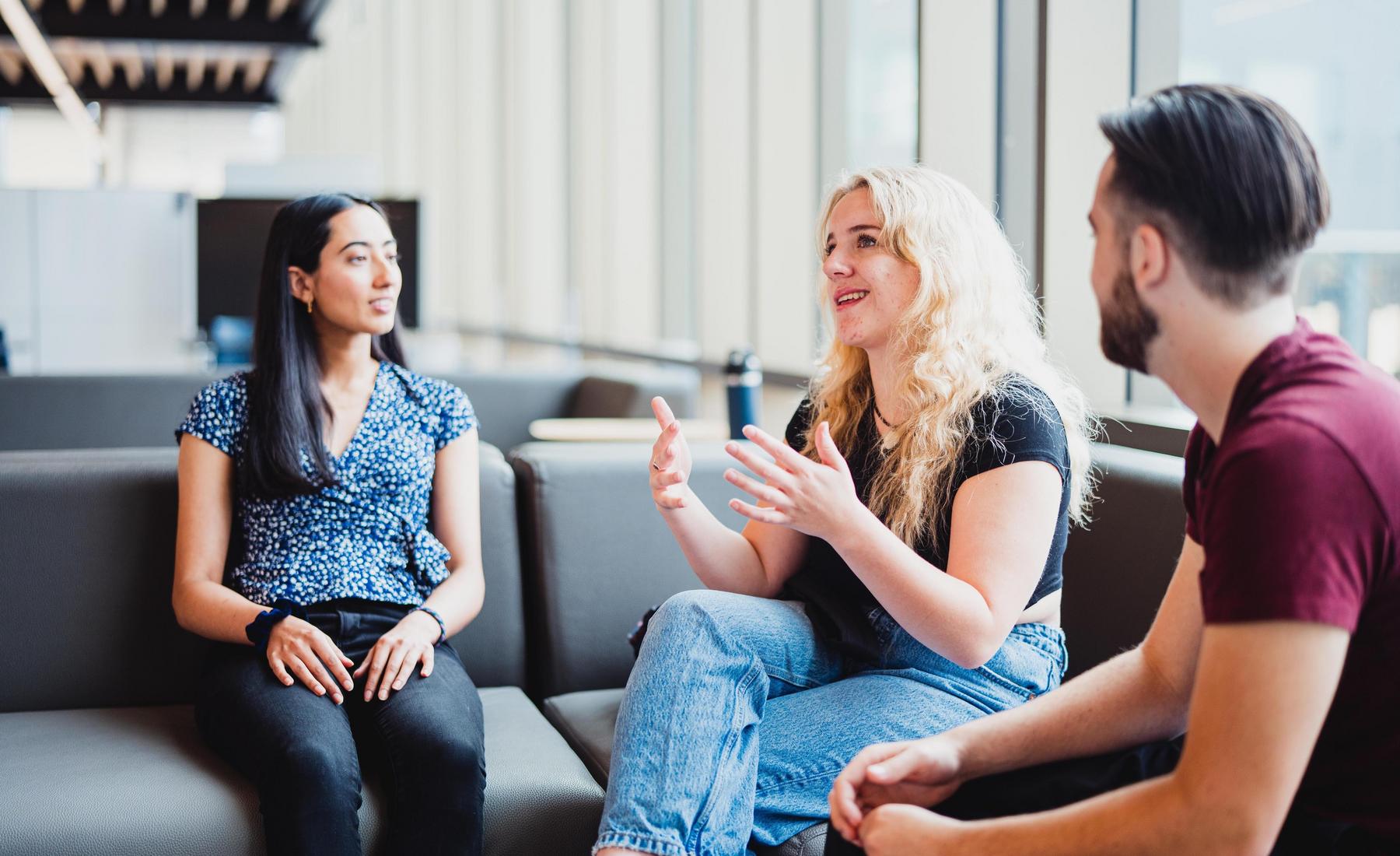 Three students sitting around and talking on couches. 