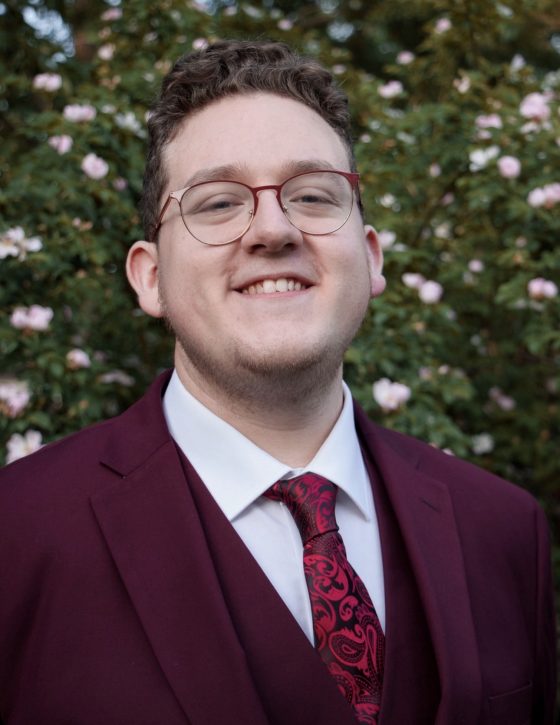 Drew Scherle standing in front of a bush with pink flowers.
