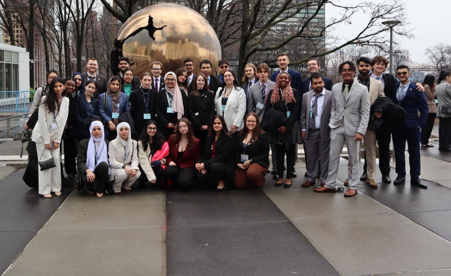 A group of 37 university students pose in front of a bronze globe statue outside the United Nations building in New York City. 