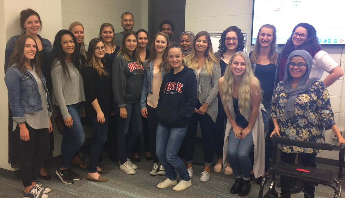 Group of nineteen people posing together at the front of a classroom.