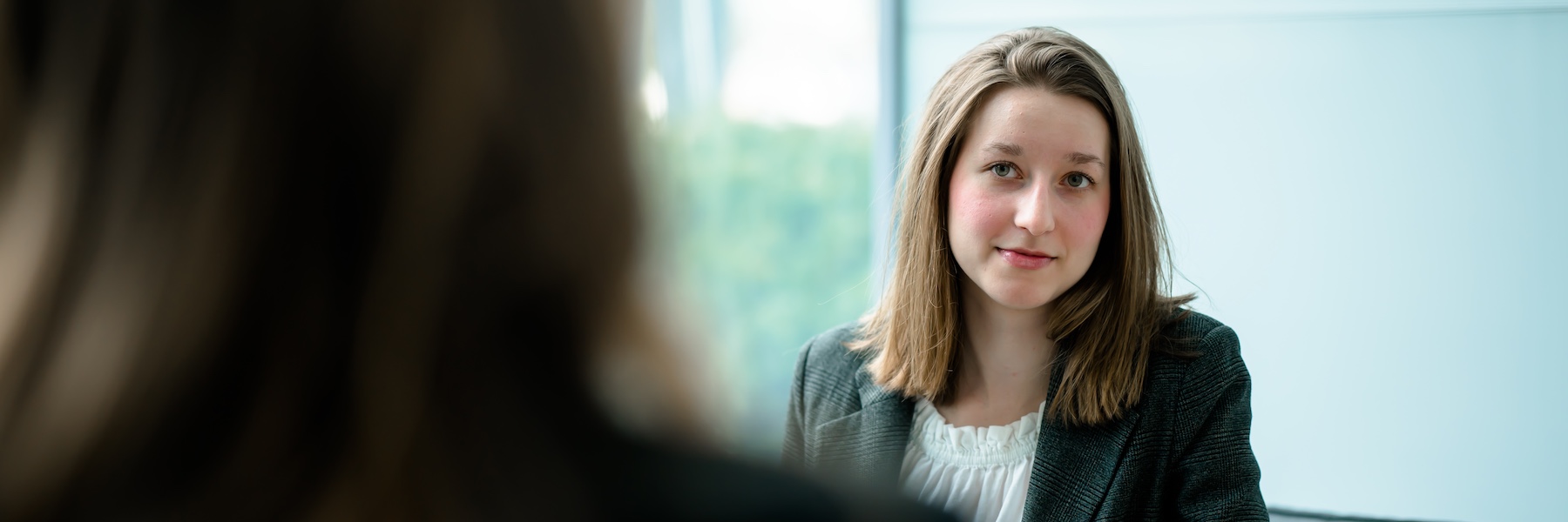 A young woman sitting near a window and looking at a person sitting across from her.