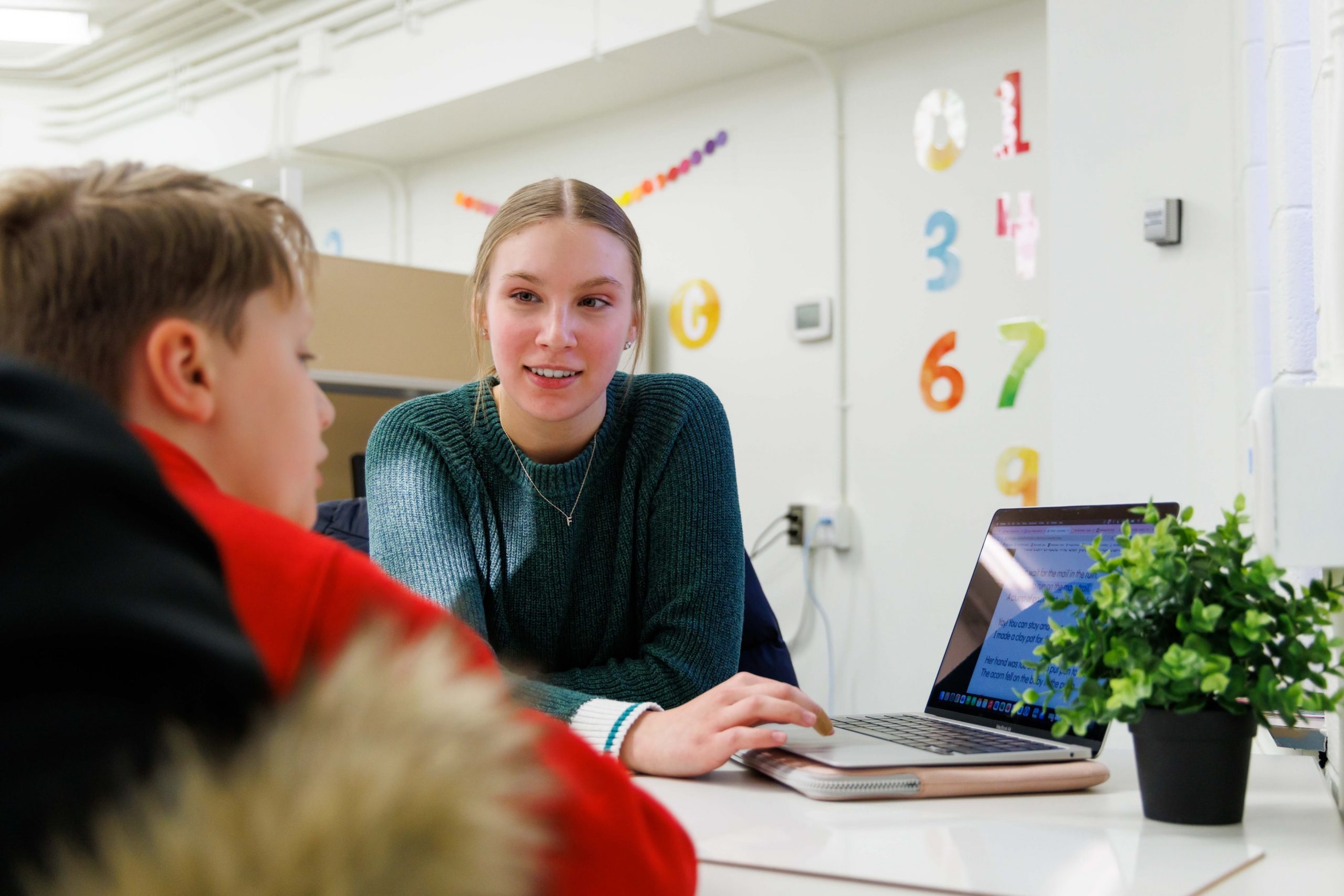 A young woman and a child sitting across from one another while looking at a laptop screen.