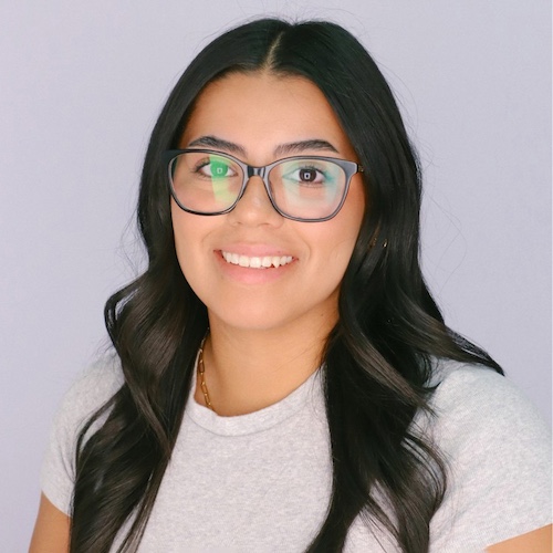 A portrait of a brunette woman wearing glasses smiling on a white backdrop.