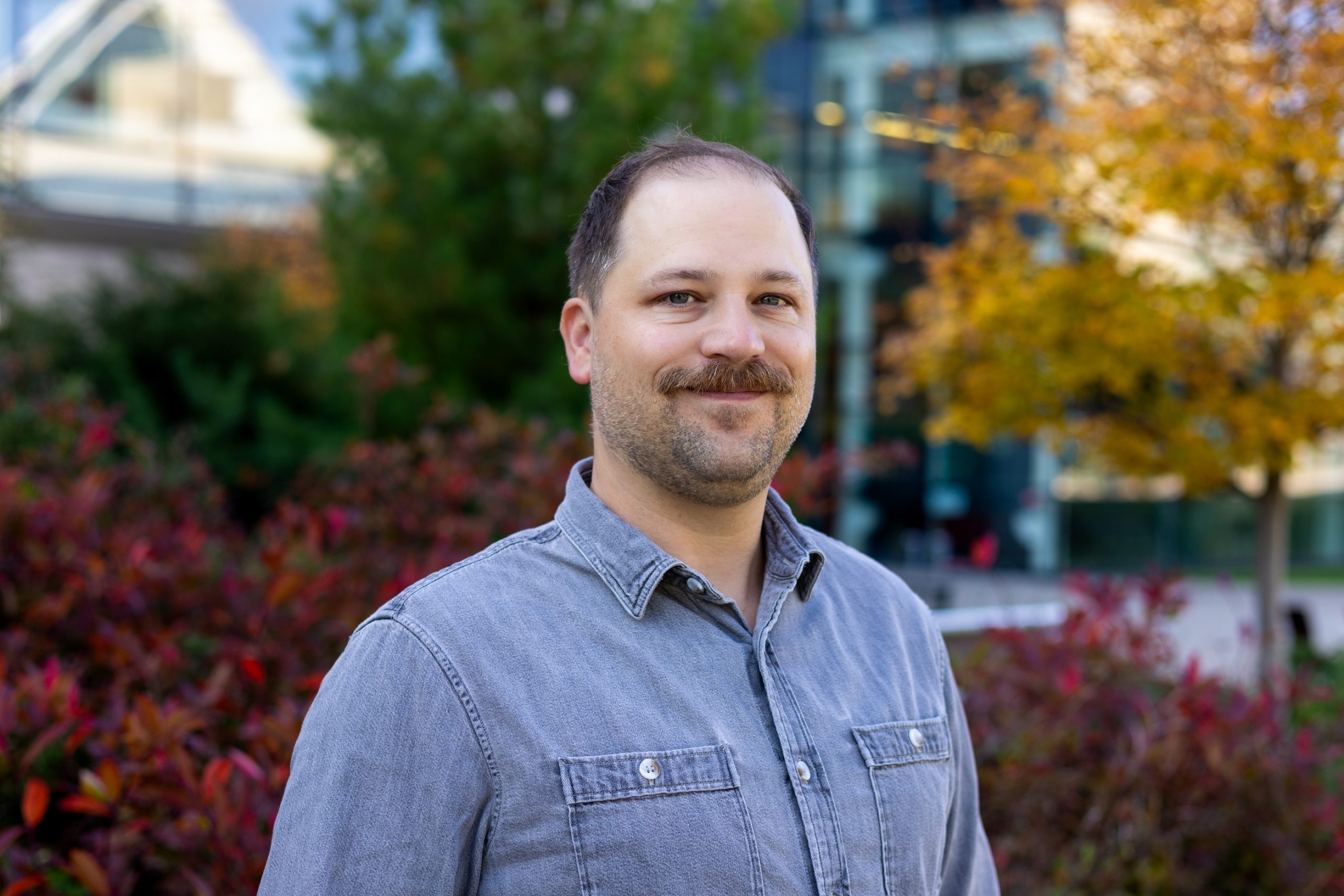 Psychology Professor Stephen Emrich standing outside with a building and fall-coloured trees in the background.