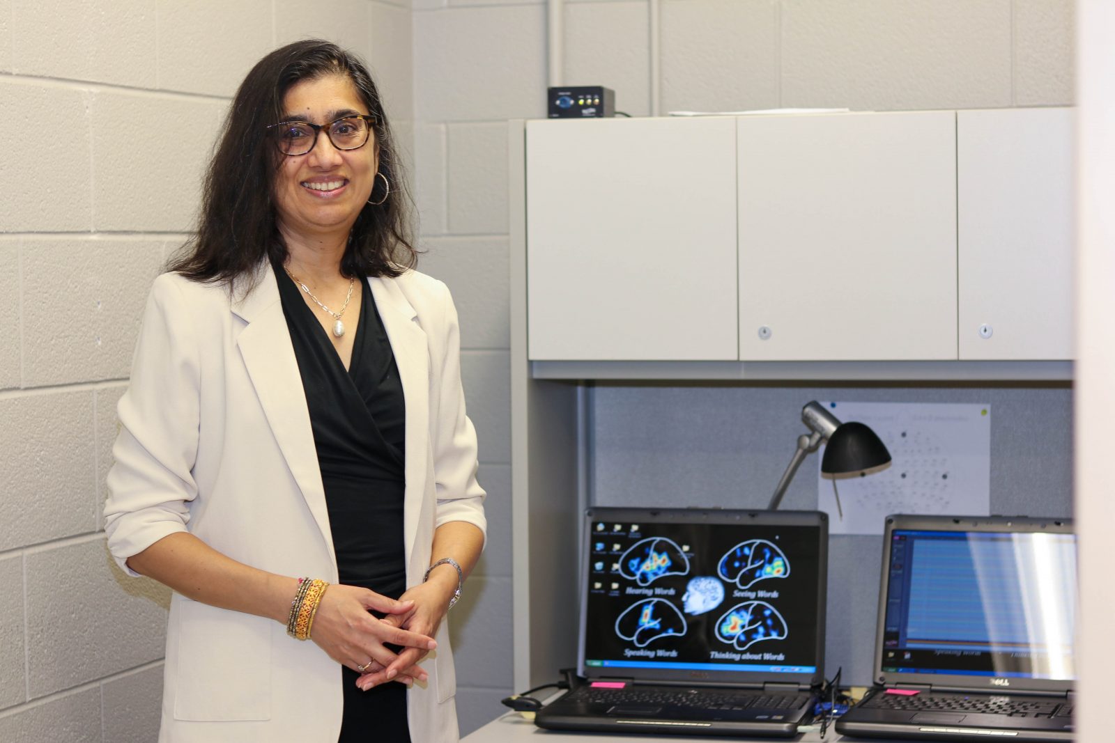 A woman standing next to two computer screens with images of brain scans and writing.