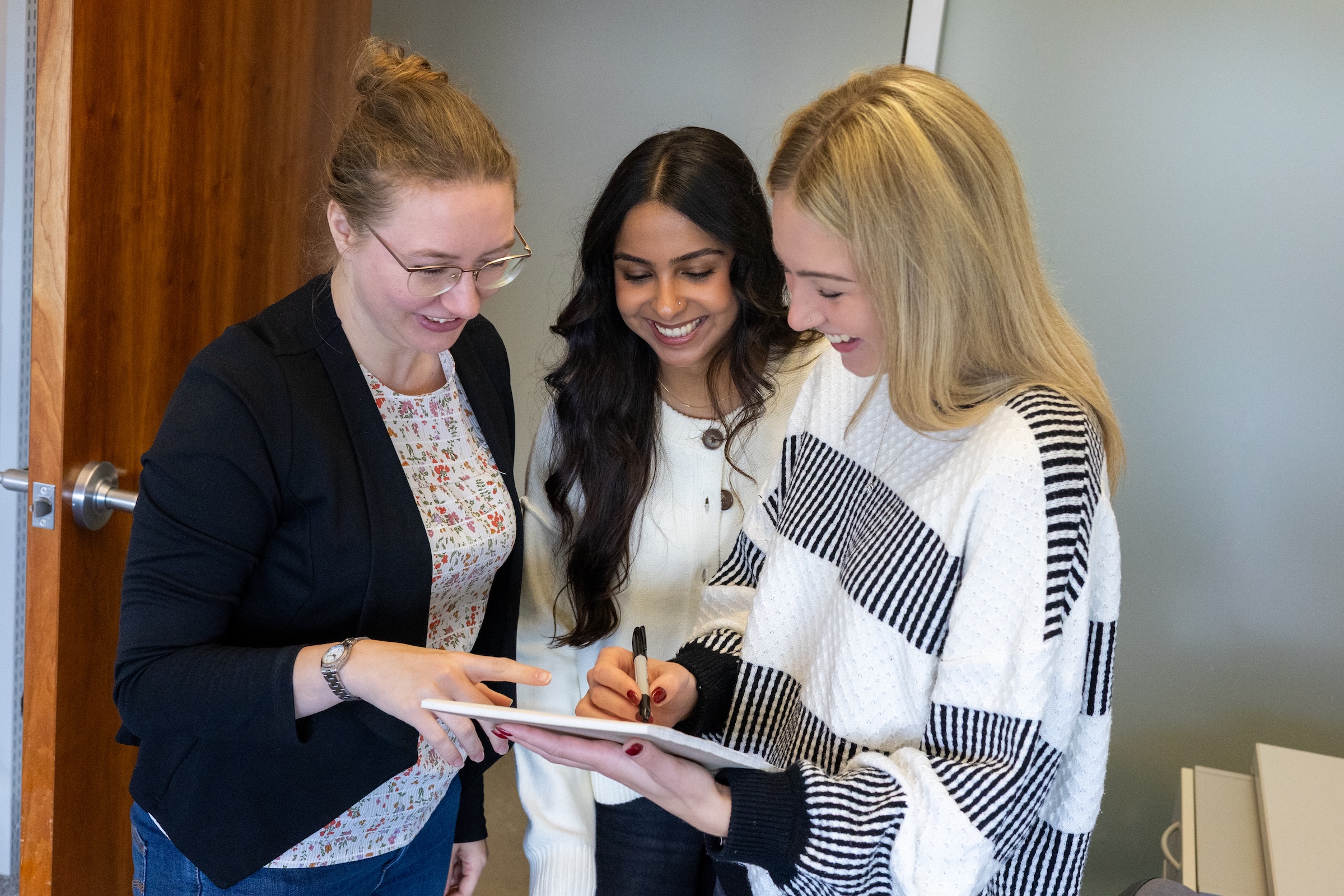Three people gathered together and looking over a notepad.
