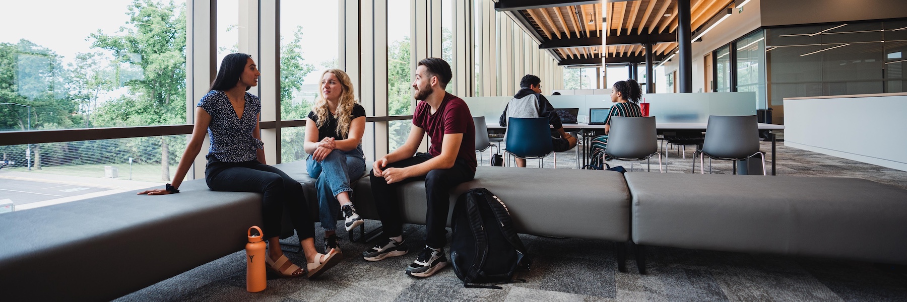 Three students sitting on couches and talking in a lounge.