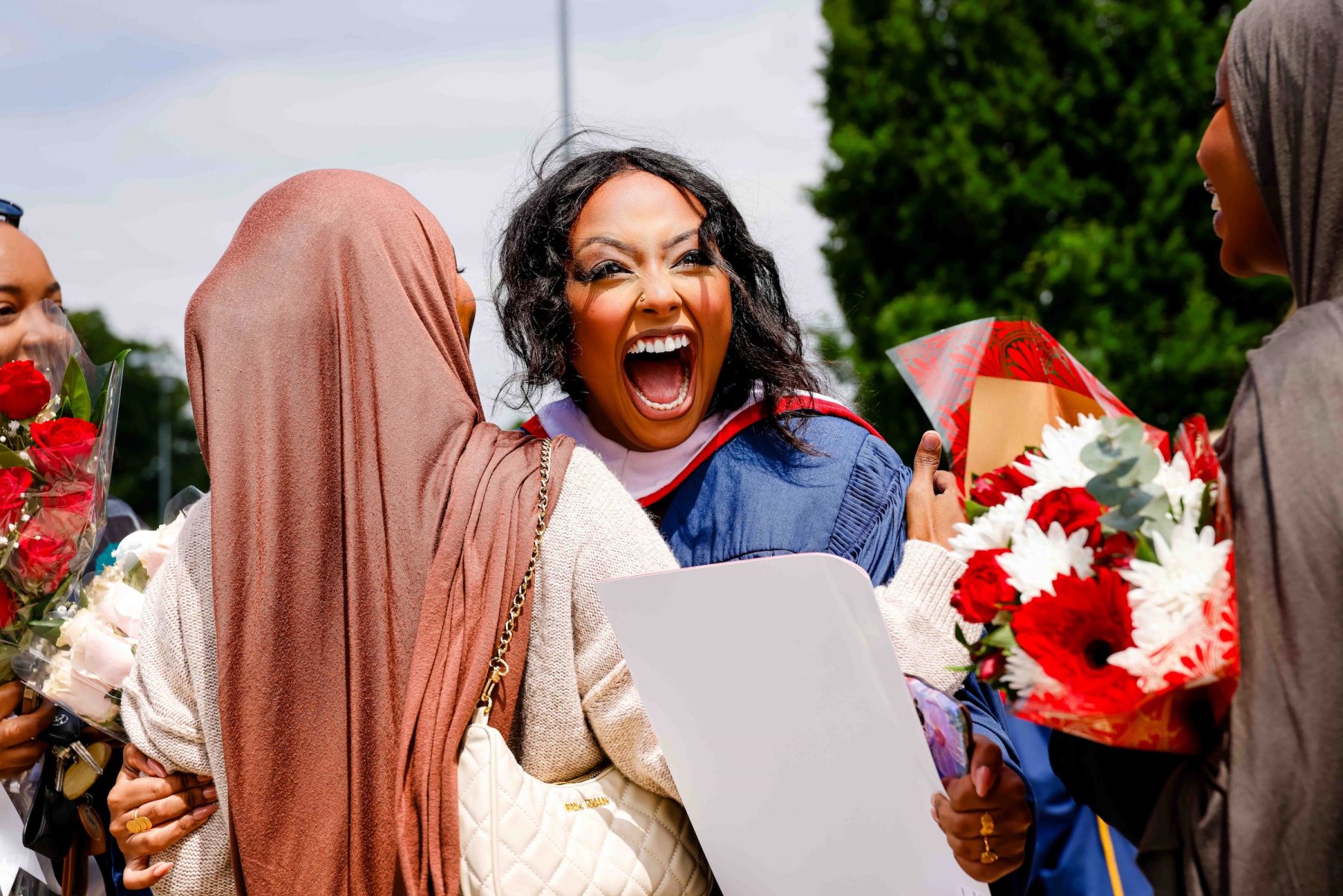 A new graduate holding a bouquet of flowers hugging someone.
