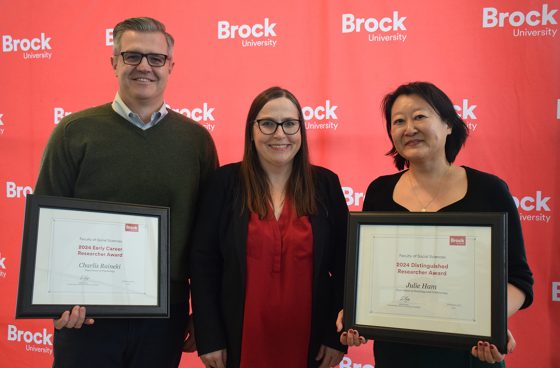 Faculty of Social Sciences Early Career Researcher Charlis Raineki, Distinguished Researcher Julie Ham and Acting Dean Dawn Zinga. Charles Raineki and Julie Ham hold framed certificates.