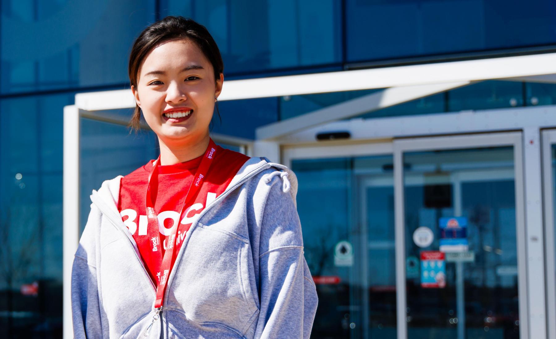 Person in a Brock University shirt standing outside on campus in front of the Rankin Family Pavilion. 