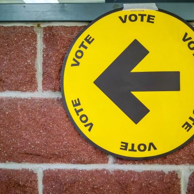 yellow voting sign on red brick wall