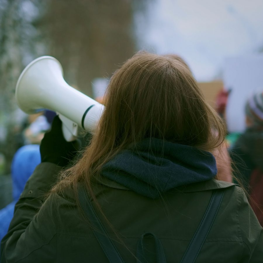 GettyImages-1766290065-copy-1600x900 A person, seen from behind, holds up a megaphone and walks down the street during a protest.