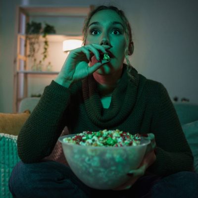 person eating popcorn watching television in the dark