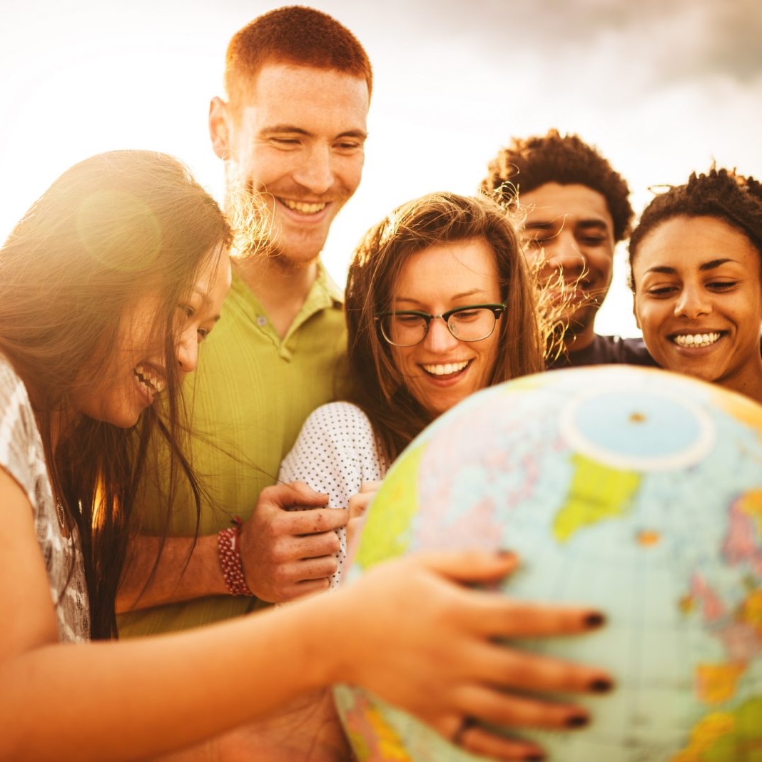 GettyImages-475871202-1600x1068 Smiling young adults hold a globe outside on a sunny day.