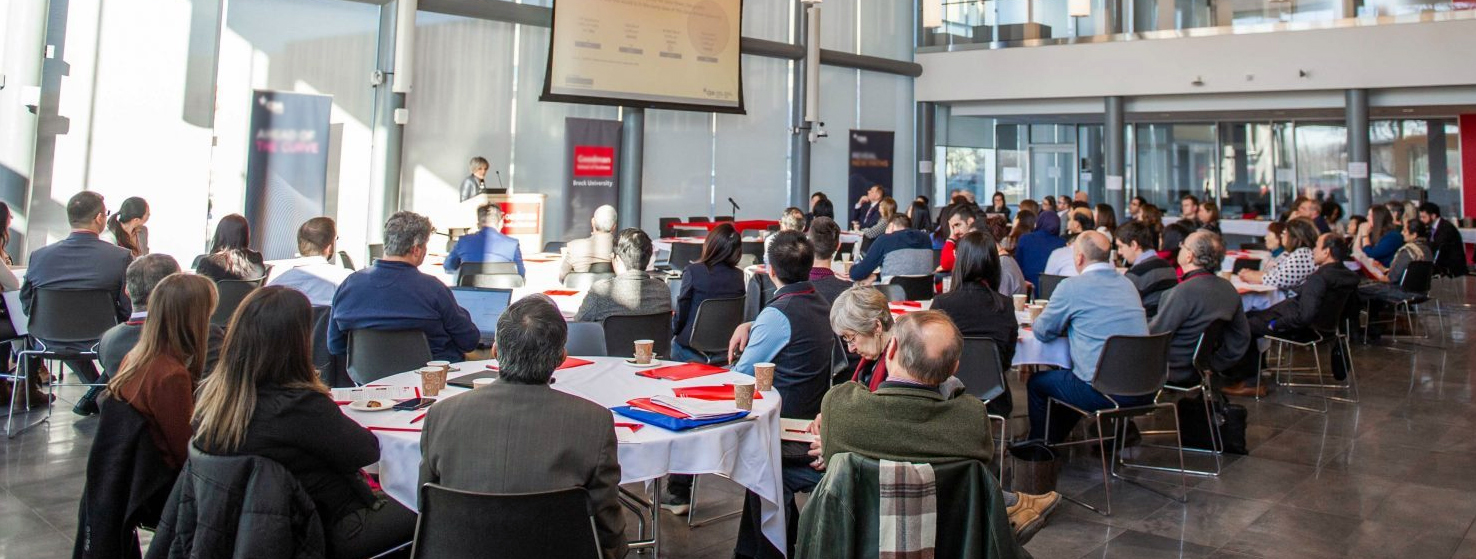Seated audience members at a presentation in Brock University's Goodman Atrium.