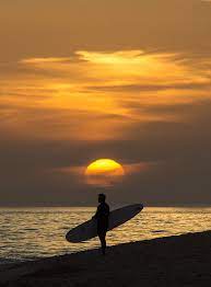 Man holding surfboard at sunset