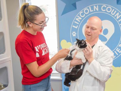 A student wearing a Brock Cares t-shirt stands next to a vet holding a cat at the Lincoln County Humane Society