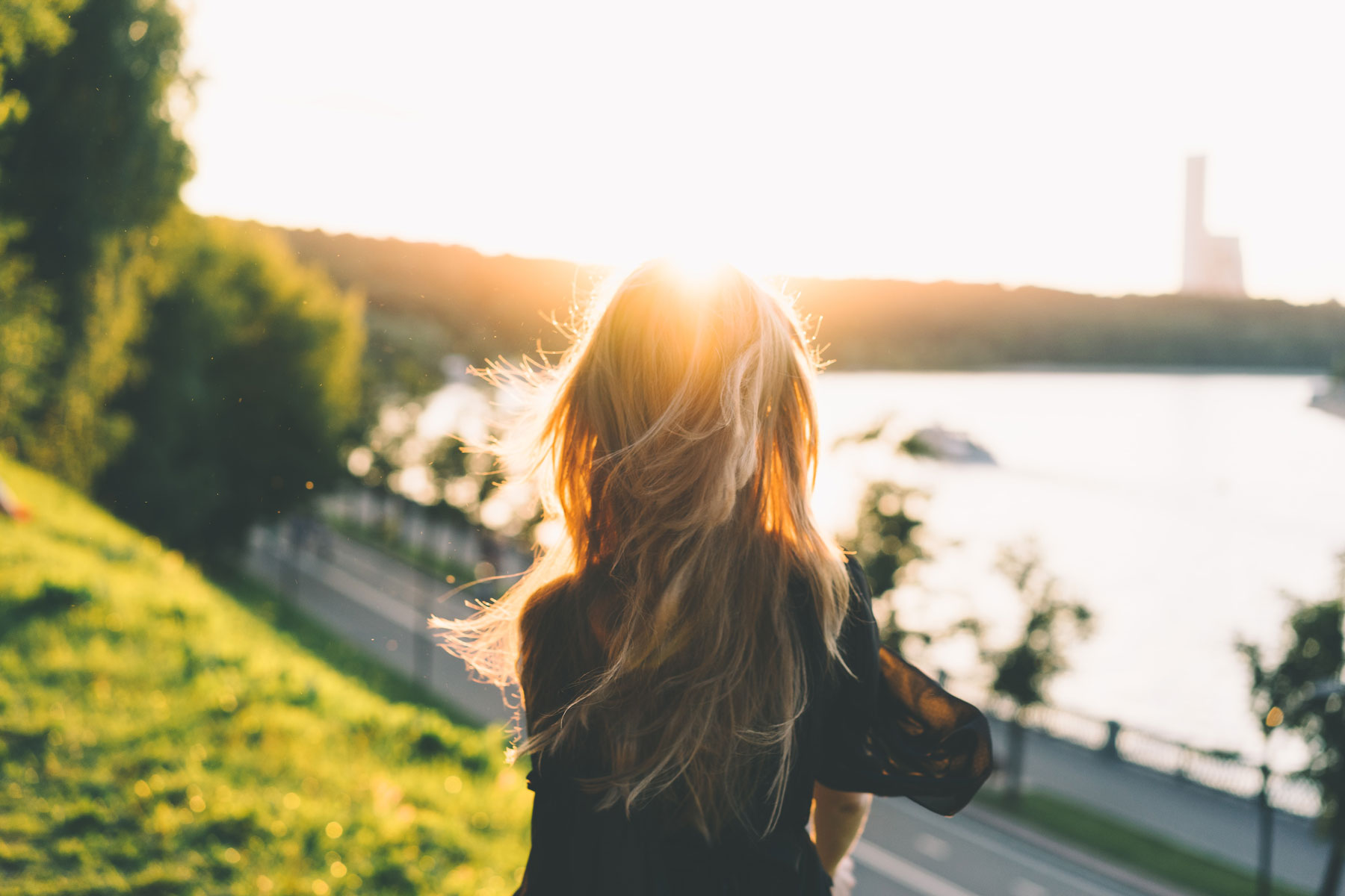 Woman sitting in the grass in a city while looking at a shoreline