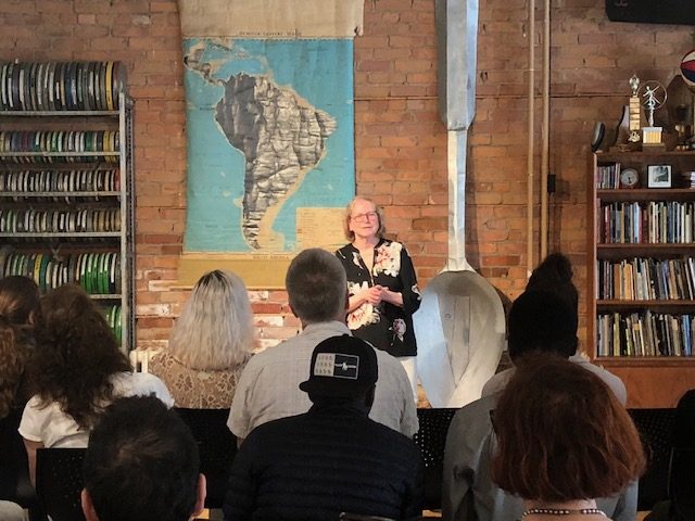 Liette Vasseur presents at an event in front of a group of seated attendees between bookcases