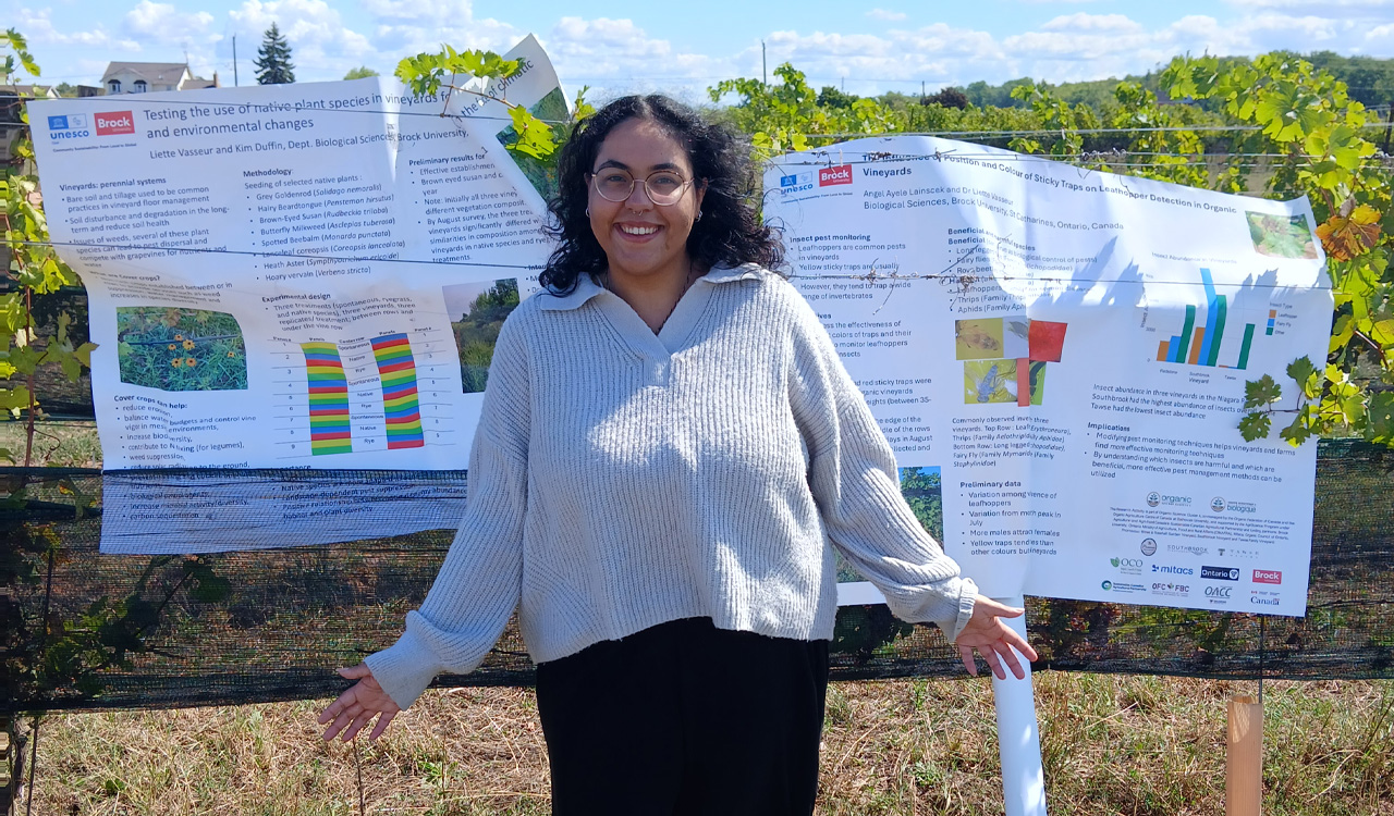 Woman stands in front of posters in a vineyard.