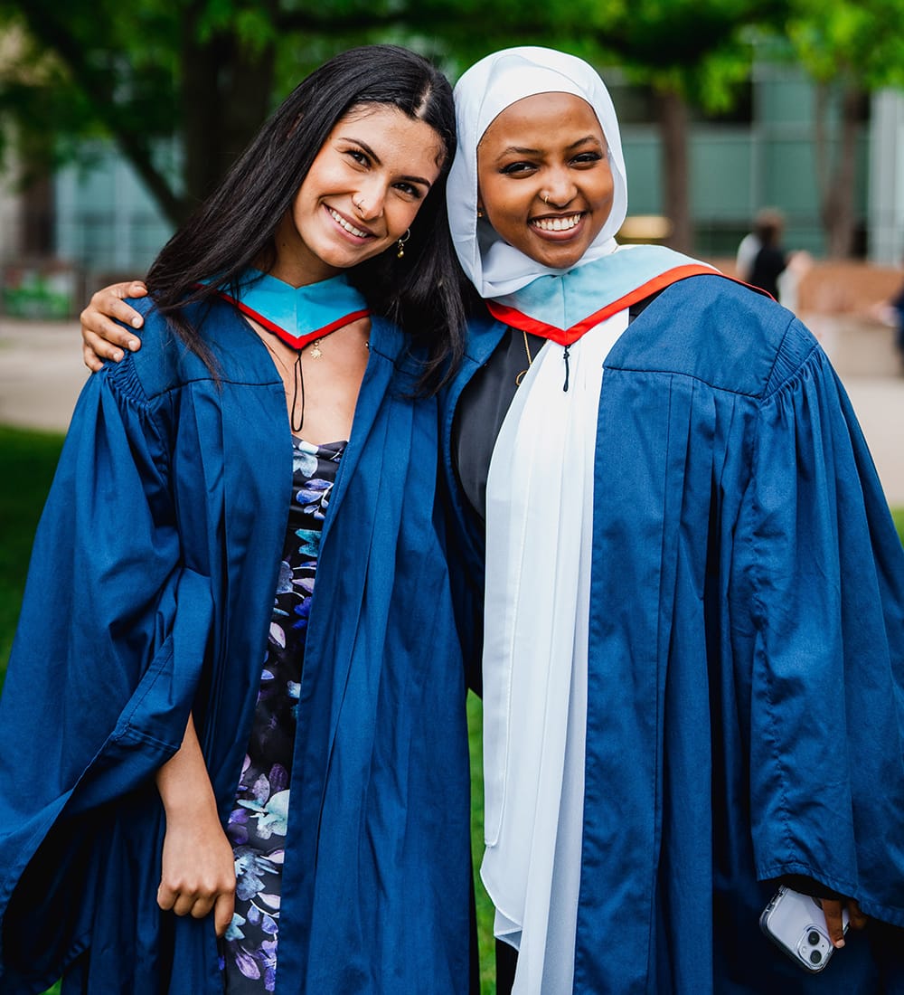 Two Brock graduates wearing graduation gowns at Convocation, smiling toward the camera. 