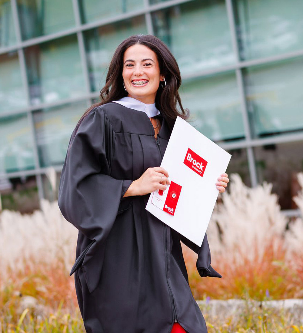 Brock graduate in gown holding her degree during the fall 2025 Convocation 