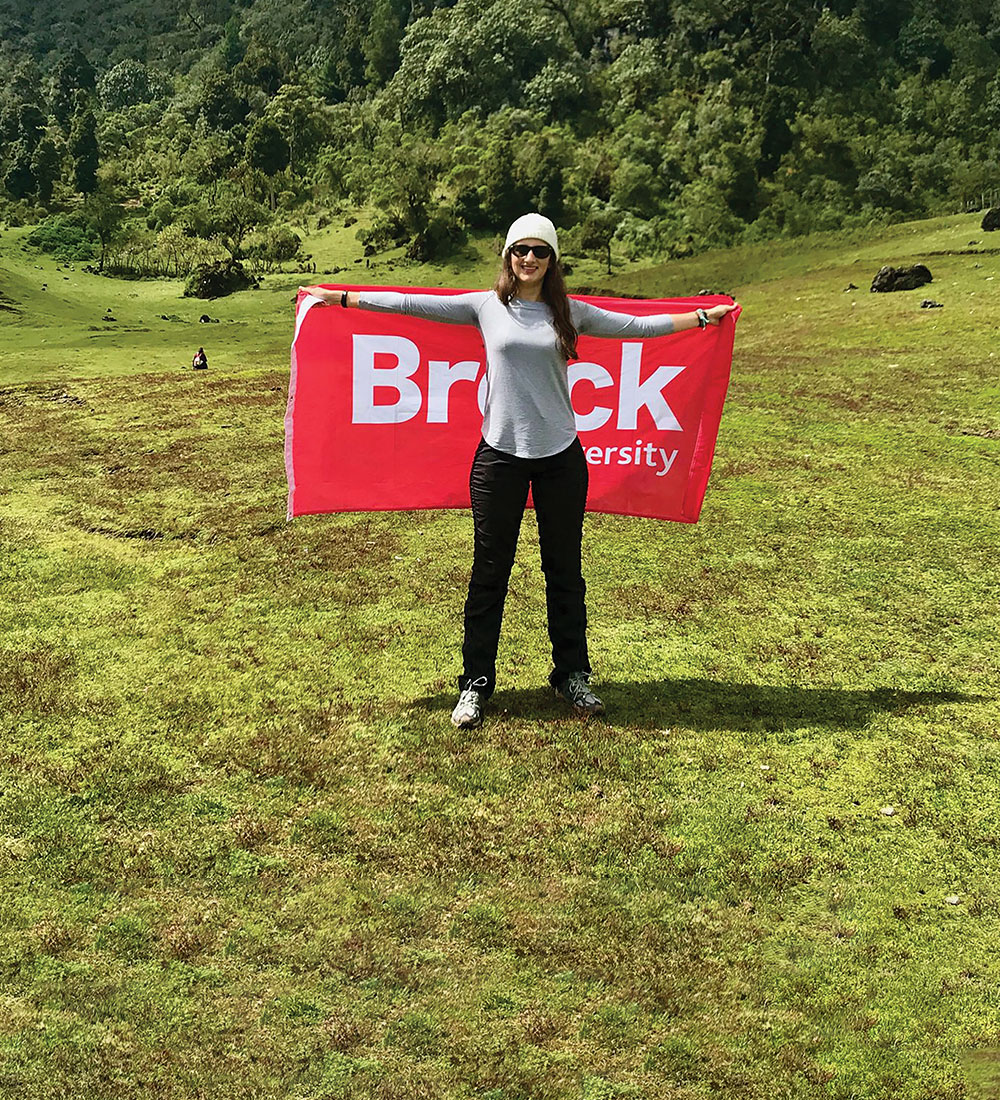 A Brock student standing in an open grassland, holding a large Brock flag. 
