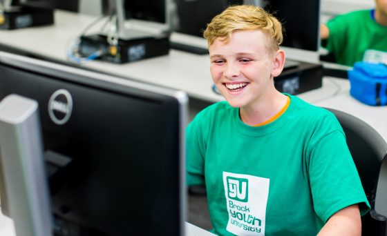 young male student laughing behind computer monitor