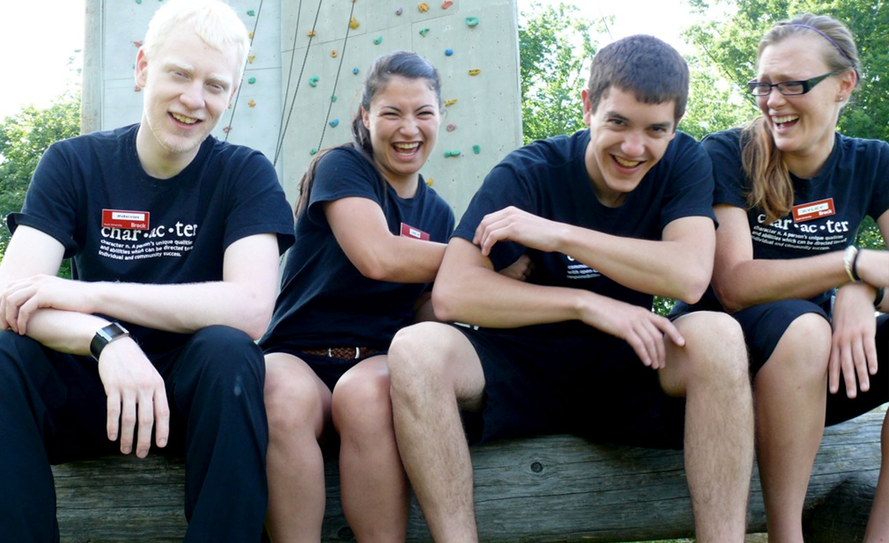Four Youth University staff sitting in front of a rock climbing wall