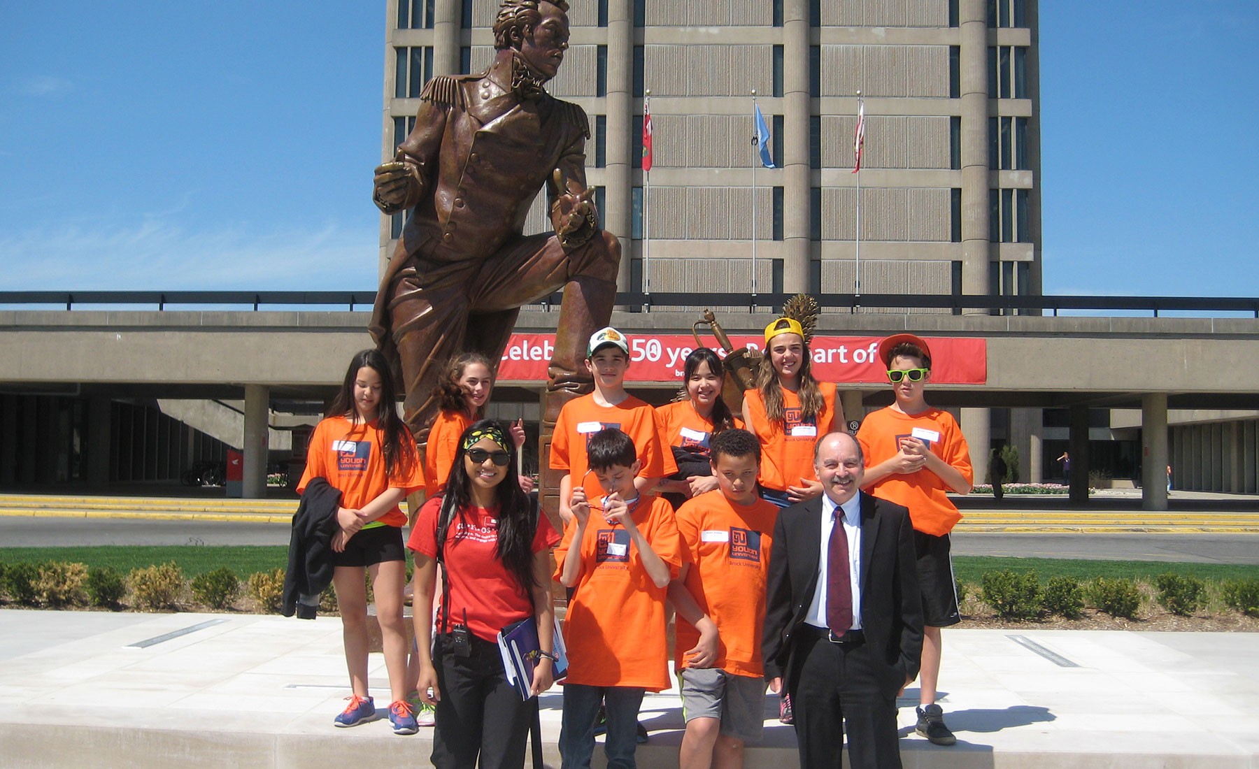 Group of young students with Brock president standing in front of Sir Isaac statue