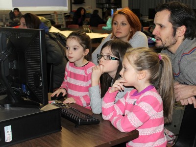 Three little girls and parents looking at a computer screen
