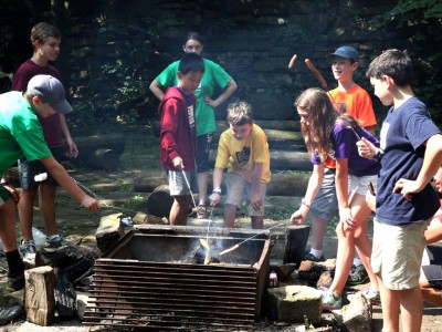Campers cooking hotdogs on outdoor fire pit